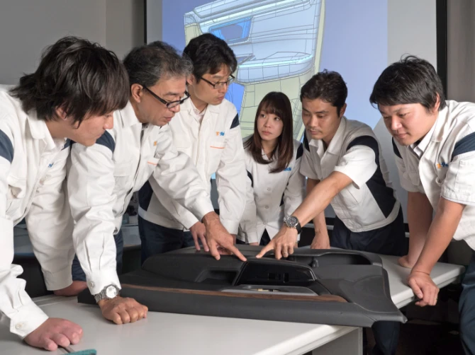 ドアトリムを囲ん触りながら議論をする6人の社員