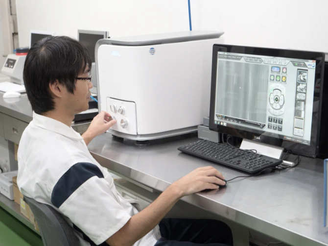 材料を試験機に入れて操作しながら、パソコンで試験の値を確認している社員